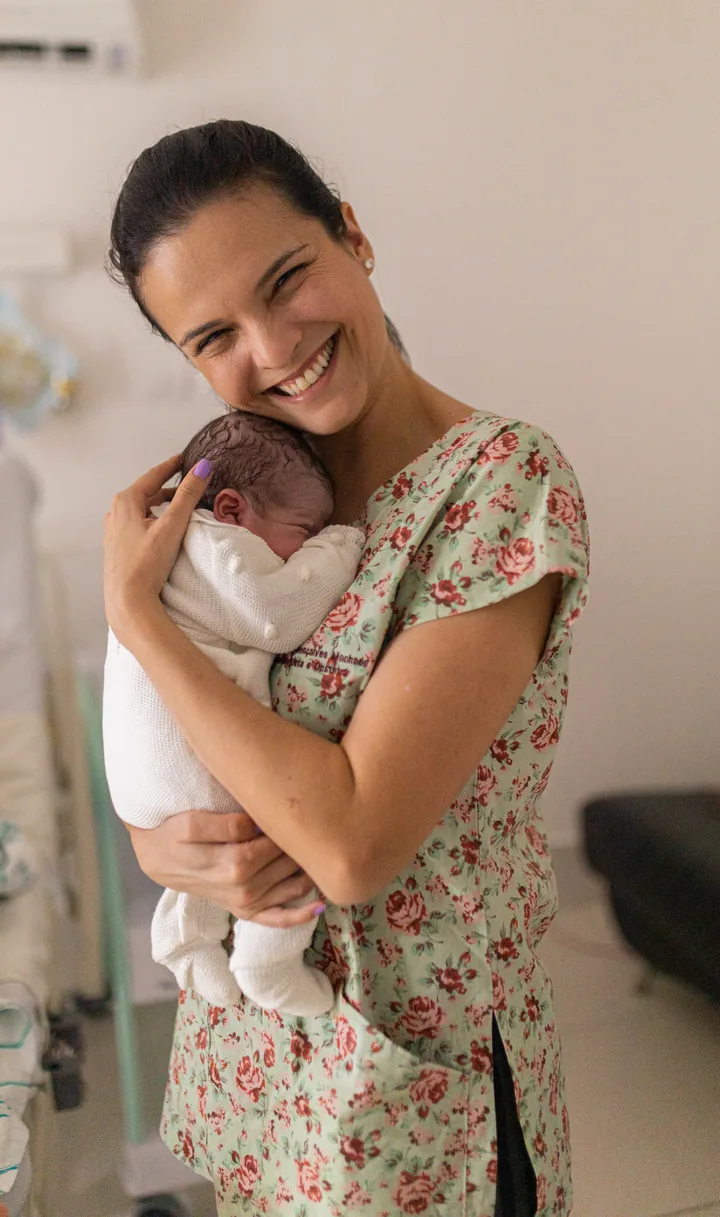 Dra. Gabriela Gonçalves Machado sorri segurando um recém-nascido